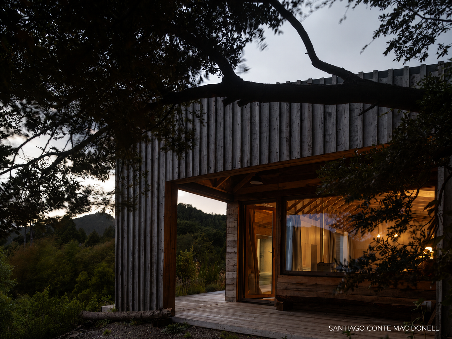 Cabaña al atardecer con ventanal de PVC iluminado y deck en el bosque
